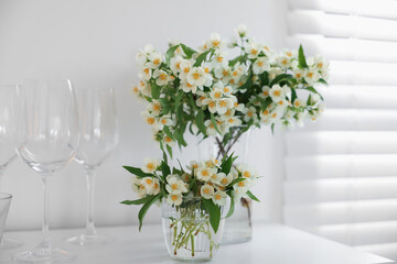 Bouquet of beautiful jasmine flowers in vase on white table indoors