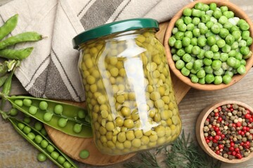 Pickled peas in jar, spices, dill and pods on wooden table, flat lay