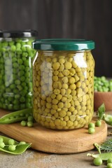 Pickled and fresh peas in jars, dill and pods on wooden table, closeup