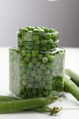 Fresh green peas in pickling jar and pods on white wooden table, closeup