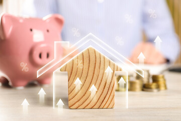 Increase in real estate value. House model, piggy bank and coins on wooden table. Growing price...
