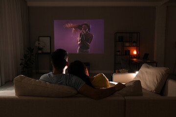Couple watching entertainment show using video projector on sofa at night