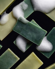 Many pieces of homemade fragrant hygienic soap in various shades of green with foam on a black background. Top view.