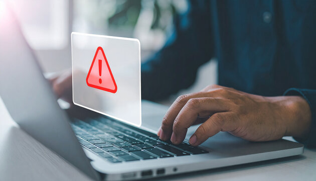 Person working on laptop with warning sign appearing on the screen.  The image shows a close up of hands typing on a laptop with a transparent warning sign.