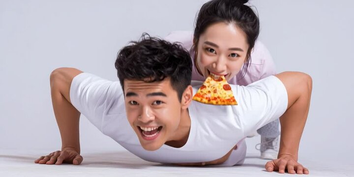 A woman is eating pizza and laughing while laying on her husband's back while he does pushups - exercise, diet, and fitness concept with a happy couple