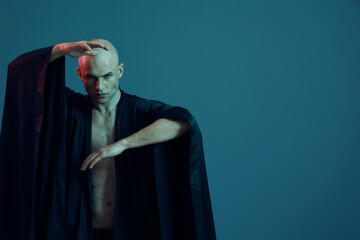 Captivating man in a flowing black robe striking a dramatic pose against a monochromatic blue...