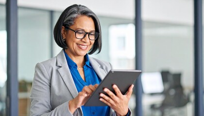 Smiling businesswoman using a tablet in a modern office. She is dressed in a smart business suit and glasses.