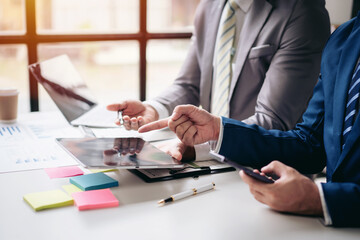 Two men in suits are looking at a tablet with a pointer