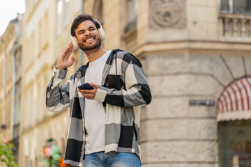 Happy overjoyed Arabian young man tourist in wireless headphones choosing, listening favorite...