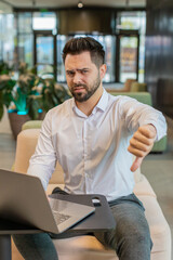 Dislike. Upset businessman guy working on laptop computer in office lobby showing thumb down sign...