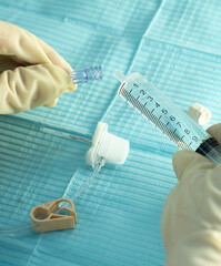 Sterile hands connecting a syringe to a Huber (gripper) needle set on a blue drape. Preparation for...