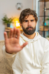 Portrait of Indian young man guy on sofa couch with serious expression doing stop gesture with hand...
