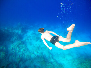 Boy snorkeling dive deep into the blue sea near the coral reef. Red Sea