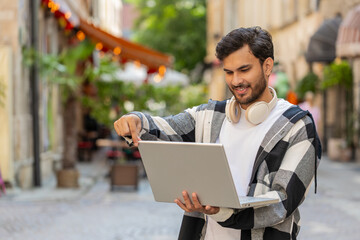 Indian man freelancer standing on street using laptop working online distant job browsing website...