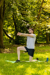 Athletic sporty fit man doing workout yoga breathing exercise on sports mat in park. Raising hands....