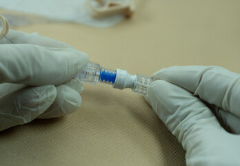 Sterile-gloved hands connecting IV tubing to a non-return cap attached to a gripper (Huber) needle....
