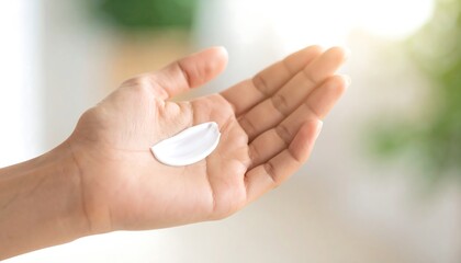 A hand holding a small dollop of white cream