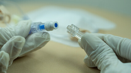 Sterile-gloved hands connecting an IV line to a non-return cap attached to a Huber (gripper)...