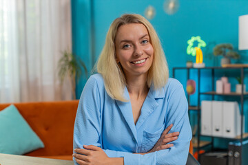 Portrait of young smiling blond Caucasian business woman at home office workplace desk looking at...
