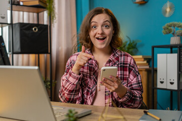 Smiling businesswoman using smartphone app online pointing showing like thumbs up remote distance...