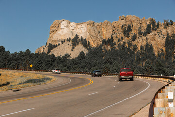A view of Mount Rushmore National Monument from Highway 244, with cars on a curve in the road, blue...