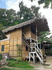 Traditional two-story bamboo house with a thatched roof, surrounded by green foliage.