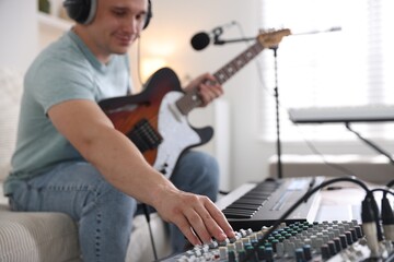 Man working with guitar, dj mixer and MIDI keyboard on sofa in home studio, selective focus