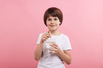 Cute little boy with glass of refreshing soda drink on pink background
