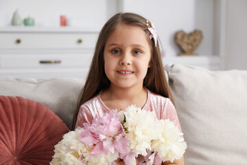 Cute little girl with bouquet of beautiful peonies on sofa at home