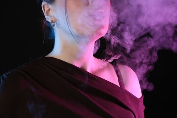 Woman using electronic smoking device in neon lights on black background, closeup
