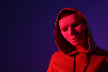 Anonymity. Woman wearing mask on dark blue background in red light, space for text