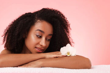 Portrait of beautiful Brazilian woman with orchid flower after spa treatment on pink gradient...