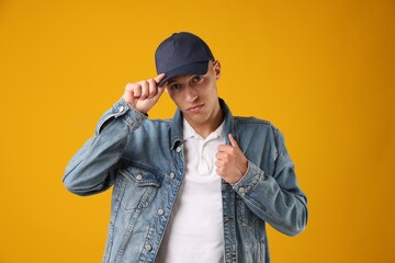 Young man in stylish baseball hat on orange background