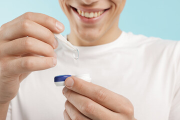 Man taking contact lens out of case on light blue background, closeup