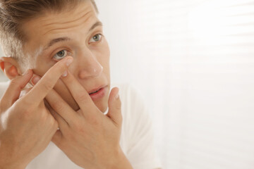 Man putting in contact lens at home, closeup. Space for text
