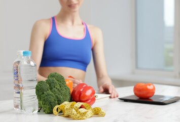 Woman developing diet plan at white marble table indoors, focus on vegetables, water and measuring...