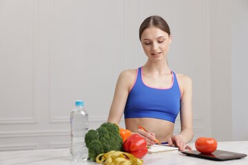 Woman developing diet plan at white marble table indoors, space for text