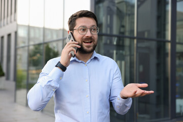 Happy businessman talking on phone near office building