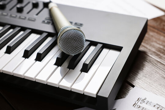 MIDI keyboard, microphone and music sheets on wooden table, closeup