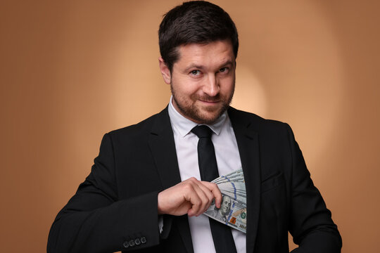 Greedy banker hiding money into inner pocket of suit on golden background