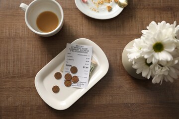 Tips, receipt, dirty plate, cup and flowers on wooden table, flat lay