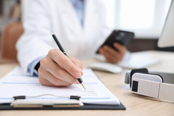 Fototapeta premium Doctor with smartphone working at table in clinic, selective focus. Online medical consultation
