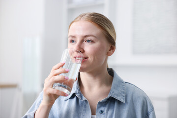 Young woman drinking water from glass at home