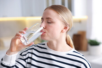 Young woman drinking water from glass in kitchen