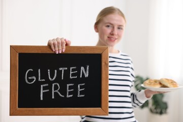 Woman holding small chalkboard with text Gluten Free and pretzels indoors, selective focus