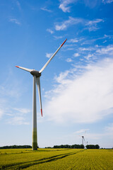 A prominent wind turbine towers over a lush green field, surrounded by a bright blue sky and soft...