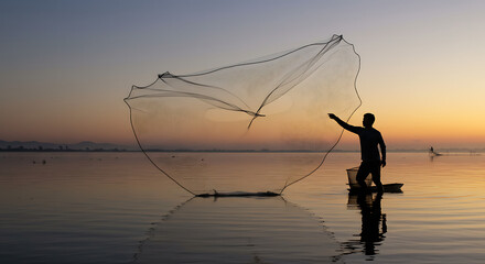 Silhouette of a fisherman casting a large fishing net at sunrise.