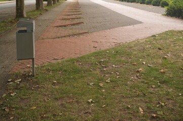 Metal trash can standing on grass next to red brick sidewalk
