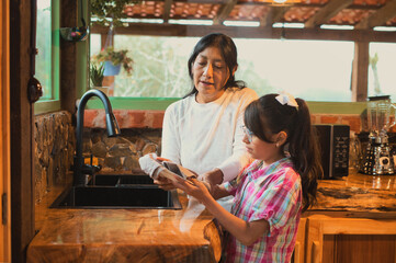 Latin american mother and daughter drying dishes in rustic kitchen