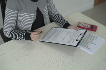 A real estate woman agent is reading and checking paper documents, signing the lease agreement,...